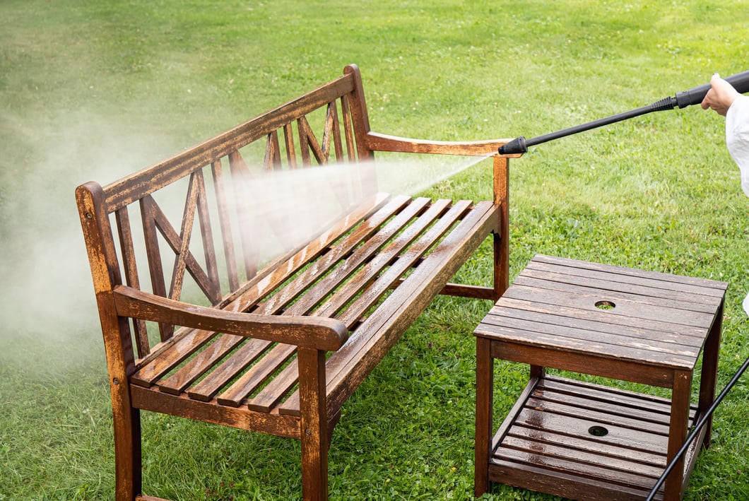 Person working cleaning pressure washing wooden garden furniture.